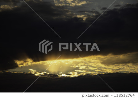 Golden sunset over calm sea with dramatic clouds and sun rays breaking through sky, warm orange horizon, tranquil ocean surface, atmospheric seascape, natural light, serene evening landscape 138532764