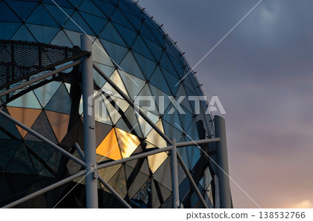 Modern glass dome architecture with geometric triangular panels and steel structure, futuristic building exterior reflecting warm sunset light, abstract urban design, minimal composition with copy spa 138532766