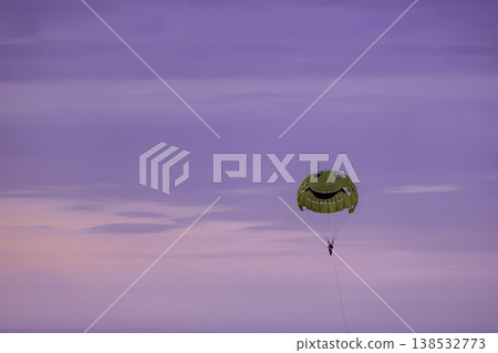 Parasailing with bright yellow smiley parachute in pastel sunset sky, lone person flying over sea horizon, minimal composition with soft gradient clouds, summer adventure and freedom concept Parasailing with bright yellow smiley parachute in pastel sunset sky, lone person flying over sea horizon, minimal composition with soft gradient clouds, summer adventure and freedom concept 138532773