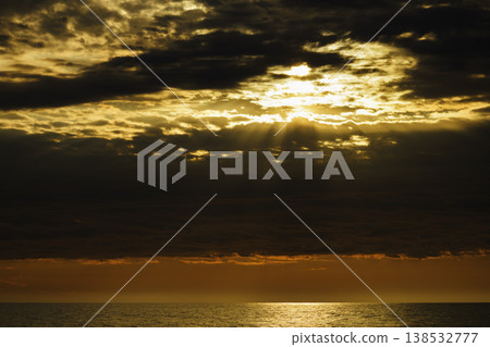 Golden sunset over calm sea with dramatic clouds and sun rays breaking through sky, warm orange horizon, tranquil ocean surface, atmospheric seascape, natural light, serene evening landscape Golden sunset over calm sea with dramatic clouds and sun rays breaking through sky, warm orange horizon, tranquil ocean surface, atmospheric seascape, natural light, serene evening landscape 138532777