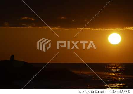Silhouette of person sitting by sea at intense red sunset with bright sun and reflection on water, dramatic sky and waves, emotional seascape with copy space, solitude and contemplation concept Silhouette of person sitting by sea at intense red sunset with bright sun and reflection on water, dramatic sky and waves, emotional seascape with copy space, solitude and contemplation concept 138532788