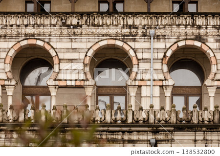 Historic stone building facade with arched windows and decorative columns, classic architecture details with symmetry and texture, old city exterior design with ornamental balcony and arches Historic stone building facade with arched windows and decorative columns, classic architecture details with symmetry and texture, old city exterior design with ornamental balcony and arches 138532800