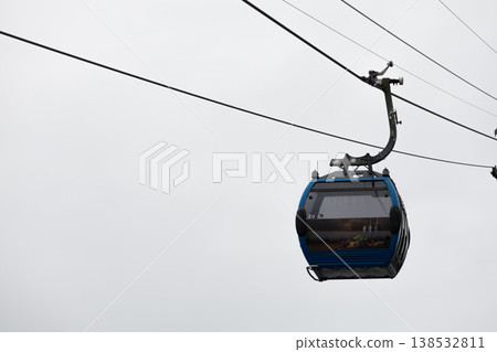 Blue cable car cabin suspended on ropeway against cloudy sky, modern gondola lift transport, minimal composition with copy space, aerial transportation concept in urban or mountain environment Blue cable car cabin suspended on ropeway against cloudy sky, modern gondola lift transport, minimal composition with copy space, aerial transportation concept in urban or mountain environment 138532811