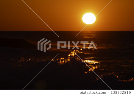 Intense red sunset over sea with bright sun and sparkling waves, dramatic reflection on water, vivid orange sky and dynamic splashes, atmospheric seascape background with strong warm tones 138532819