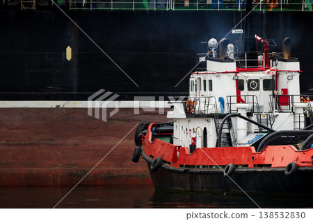 Tugboat assisting large cargo vessel in harbor, maritime transport and port operations, industrial shipping logistics scene with powerful tug pushing ship hull on calm water Tugboat assisting large cargo vessel in harbor, maritime transport and port operations, industrial shipping logistics scene with powerful tug pushing ship hull on calm water 138532830