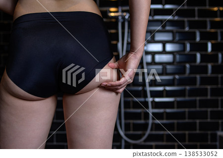 A young woman pinches the excess fat on her slightly chubby buttocks; she's just starting to gain weight; she's in the bath. 138533052