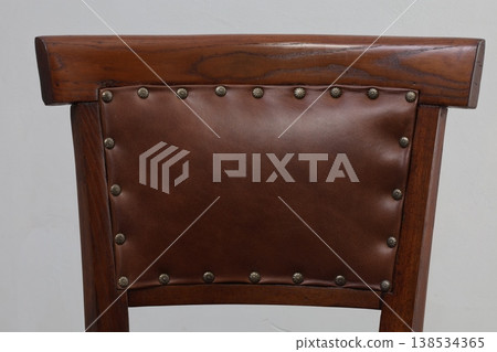 Elegant wooden chair featuring rich leather backrest with decorative studs in a soft-lit interior space Elegant wooden chair featuring rich leather backrest with decorative studs in a soft-lit interior space 138534365