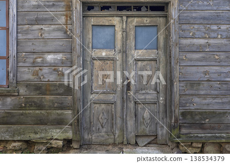 Weathered wooden door captures the essence of forgotten stories in a rustic building under a peaceful blue sky Weathered wooden door captures the essence of forgotten stories in a rustic building under a peaceful blue sky 138534379