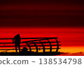 Silhouette of fisherman on pier at sunset over sea, dramatic red sky and ocean horizon, peaceful fishing scene, solitude and lifestyle concept with calm evening atmosphere 138534798