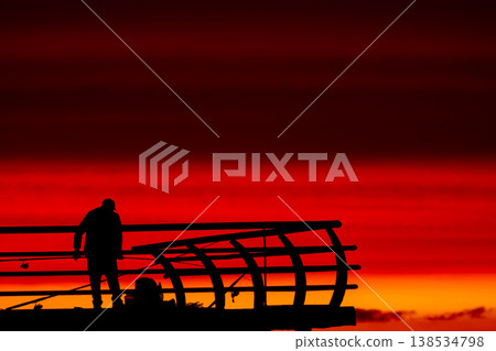 Silhouette of fisherman on pier at sunset over sea, dramatic red sky and ocean horizon, peaceful fishing scene, solitude and lifestyle concept with calm evening atmosphere Silhouette of fisherman on pier at sunset over sea, dramatic red sky and ocean horizon, peaceful fishing scene, solitude and lifestyle concept with calm evening atmosphere 138534798