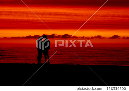 Silhouette of couple embracing at sunset by the sea, romantic scene with dramatic red sky and ocean horizon, love and relationship concept, peaceful evening atmosphere and nature background 138534800