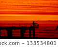 Silhouette of fisherman on pier at sunset over sea, dramatic red sky and ocean horizon, peaceful fishing scene, solitude and lifestyle concept with calm evening atmosphere 138534801