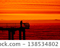 Silhouette of fisherman on pier at sunset over sea, dramatic red sky and ocean horizon, peaceful fishing scene, solitude and lifestyle concept with calm evening atmosphere 138534802