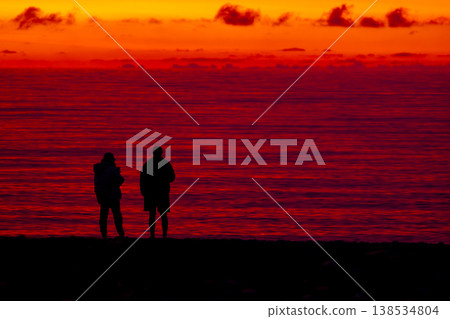 Silhouette of couple embracing at sunset by the sea, romantic scene with dramatic red sky and ocean horizon, love and relationship concept, peaceful evening atmosphere and nature background 138534804