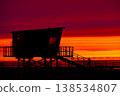 Silhouette of lifeguard tower on beach at dramatic red sunset, coastal structure with stairs and pier, ocean horizon in background, minimalistic evening scene with vivid sky and travel mood 138534807