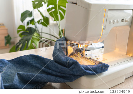 Sewing machine working on heavy denim, preparing a garment. Crafting and tailoring hobby at home atelier Sewing machine working on heavy denim, preparing a garment. Crafting and tailoring hobby at home atelier 138534949