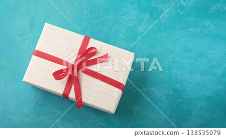 Gift box. Holiday surprise. Wrapped present package with red ribbon bow on blue festive textured background with empty space. Gift box. Holiday surprise. Wrapped present package with red ribbon bow on blue festive textured background with empty space. 138535079