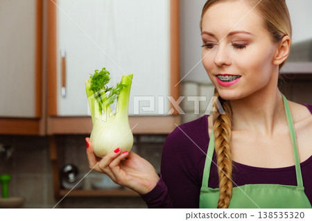 Woman in kitchen holds raw fennel bulb vegetable 138535320