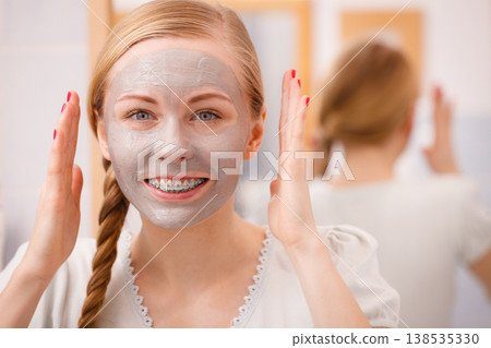 Happy young woman having mud mask on face 138535330