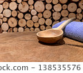 Wooden sauna ladle and blue towel on rustic wood table with stacked log background for spa wellness relaxation 138535576