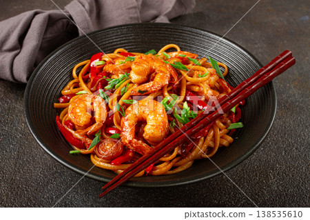 udon stir-fry shrimp noodles with red bell pepper and green onion, served in a black bowl, with chopsticks, dark background, 138535610