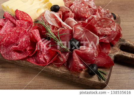 Assorted meat, appetizer, prosciutto, salami and ham, with maasdam cheese and olives, on a wooden board, breakfast, top view, close-up, no people Assorted meat, appetizer, prosciutto, salami and ham, with maasdam cheese and olives, on a wooden board, breakfast, top view, close-up, no people 138535616