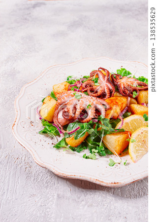 Grilled octopus with baked potatoes and fresh herbs, on a decorative light plate, homemade, no people 138535629