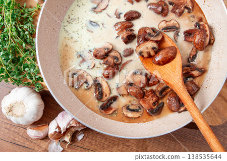 Mushrooms cooking in cream sauce with garlic and herbs on a wooden table Mushrooms cooking in cream sauce with garlic and herbs on a wooden table 138535644