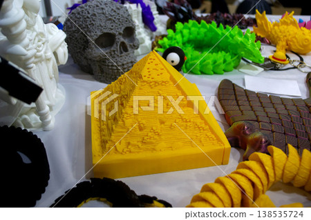 3D printed different art objects. Objects printed on 3D printer from melted colored plastic. Model yellow pyramid created on 3D printer from threads of molten plastic. Modern additive technologies 138535724
