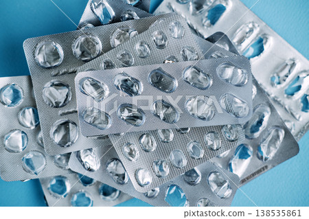 Collection of used medication blister packs lies scattered on blue surface. Non-recyclable medical waste, plastic pollution in healthcare, eco-friendly pharmacy trends. Collection of used medication blister packs lies scattered on blue surface. Non-recyclable medical waste, plastic pollution in healthcare, eco-friendly pharmacy trends. 138535861
