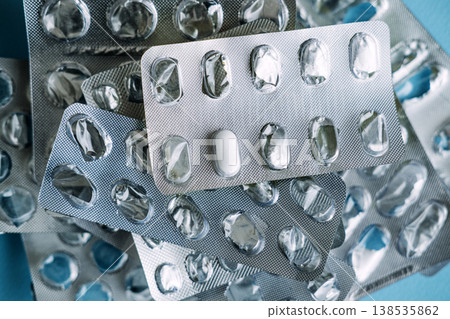 Single white tablet remains in silver blister pack among empty medication wrappers. Chronic disease management, long-term medication use, daily treatment routine. 138535862