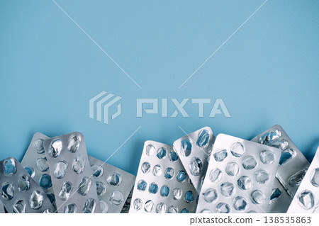 Empty silver blister packs line bottom edge of blue surface with copy space above. Cost of staying healthy, healthcare accessibility issues, financial weight of treatment. 138535863