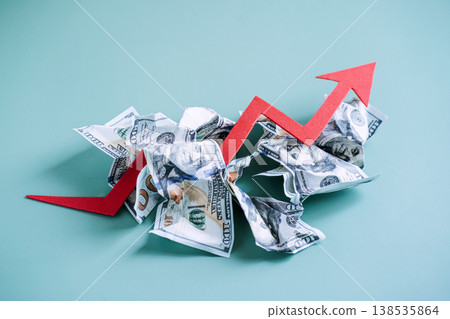 Red arrow trends upward through pile of crumpled dollar bills on blue background. Global inflation rates, rising consumer prices, economic growth trend. Red arrow trends upward through pile of crumpled dollar bills on blue background. Global inflation rates, rising consumer prices, economic growth trend. 138535864