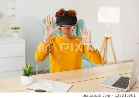 African American young woman wearing using virtual reality metaverse VR glasses headset at home. Girl touching air during VR experience on virtual reality helmet. Simulation hi-tech videogame concept African American young woman wearing using virtual reality metaverse VR glasses headset at home. Girl touching air during VR experience on virtual reality helmet. Simulation hi-tech videogame concept 138536501
