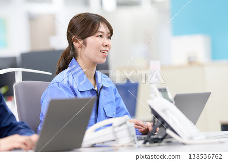 A smiling female staff member in work clothes performs data entry. A smiling female staff member in work clothes performs data entry. 138536762