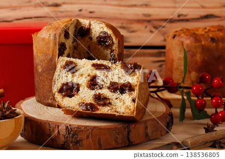 Slice of artisanal panettone filled with chocolate chips or chocotone on a white plate on a rustic table in selective focus. Christmas dessert and family dinner Slice of artisanal panettone filled with chocolate chips or chocotone on a white plate on a rustic table in selective focus. Christmas dessert and family dinner 138536805