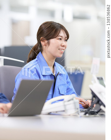 A smiling female staff member in work clothes performs data entry. 138536862