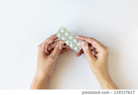 Woman's hands carefully hold a blister pack containing blue pills, preparing to remove a pill. Woman's hands carefully hold a blister pack containing blue pills, preparing to remove a pill. 138537627