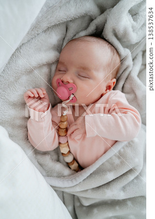 Baby resting comfortably indoors with pacifier clip. Concept of newborn care, safety and calm sleep in home environment. Baby resting comfortably indoors with pacifier clip. Concept of newborn care, safety and calm sleep in home environment. 138537634