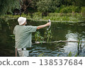 Man with fishing rod near the lake fishing at summer. Fisherman catch a fish. Man wearing khaki clothes and a cap. 138537684