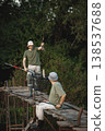 Father and adult son with fishing rods near the lake fishing at summer. Fishermen sitting on a footbridge. Men wearing khaki clothes and a caps. 138537688