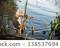 Man with fishing rod near the lake fishing at summer. Fisherman enjoying his hobby. Man wearing khaki clothes and a cap. 138537694