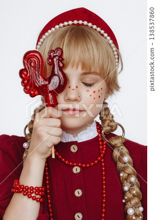 Smiling Caucasian girl with rooster lollipop in Russian folk style outfit on light background 138537860