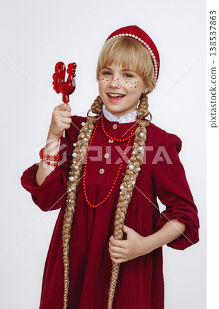 Smiling Caucasian girl with rooster lollipop in red folk style dress on light background Smiling Caucasian girl with rooster lollipop in red folk style dress on light background 138537863