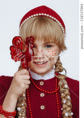 Smiling Caucasian girl with rooster lollipop in Russian folk style outfit on light background 138537864