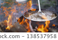 Cast-iron cauldron with soup at the stake in the courtyard. Summer day and dinner in the fresh air near the flower bed. Homemade bricks with cast iron lid. Cast iron with soup at the stake. 138537958