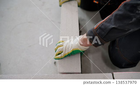 A construction worker's gloved hand laying an autoclaved aerated concrete block to build an interior wall. 138537970