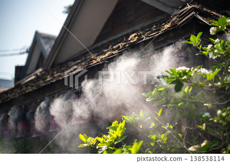 Refreshing mist spraying outside house from roof on hot summer day, water vapor spraying technology. Refreshing mist spraying outside house from roof on hot summer day, water vapor spraying technology. 138538114