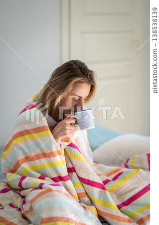Relaxed woman drinking coffee sitting on comfy bed in cozy bedroom in rays of morning sunshine. 138538139