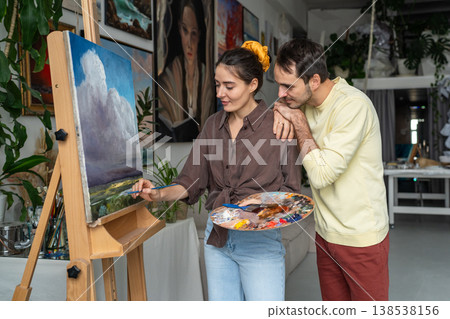 Creative couple enjoying painting, curious husband watching wife drawing oil landscape on canvas. Creative couple enjoying painting, curious husband watching wife drawing oil landscape on canvas. 138538156